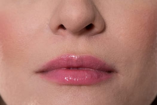 A closeup shot showcasing glossy lips that feature a stunning shimmering finish along with soft blush tones