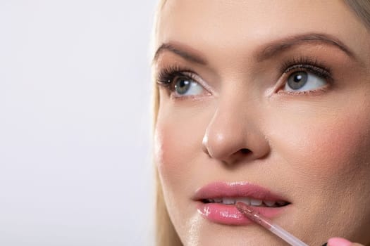 A closeup view of a woman diligently applying a shiny lip gloss, which showcases a glamorous and stunning makeup look