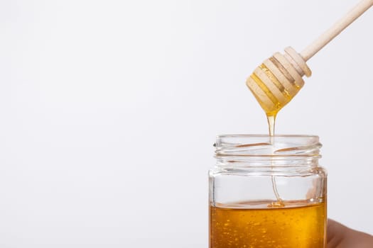 This is a closeup shot showcasing golden honey flowing gracefully from a wooden dipper into a glass jar