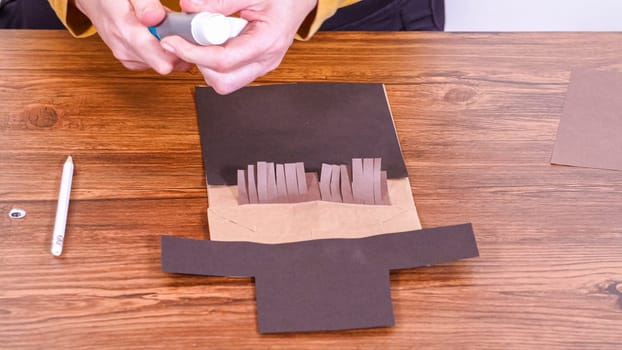 Step by step. Teacher guides online class through making a paper puppet from a brown bag, creatively using a wooden surface as a workspace.