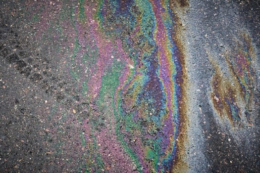Gasoline or oil spill showing iridescent colors on asphalt road surface.