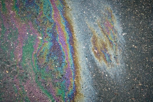 Colorful gasoline or oil spill creating a rainbow effect on asphalt road, illustrating pollution and environmental damage.