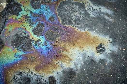 The asphalt road surface displays a beautiful rainbow sheen caused by a gasoline or oil spill.