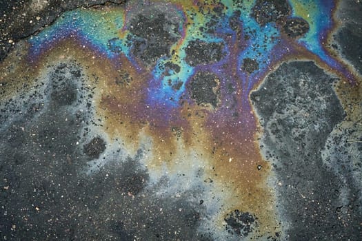 Vibrant rainbow sheen emerges on the asphalt surface as a result of an oil or gasoline spill.