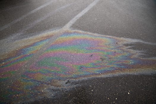 Gasoline or oil spill creating rainbow sheen on damaged asphalt parking lot.