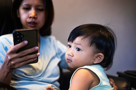 Little boy sitting near his mother working online with smartphone at home.