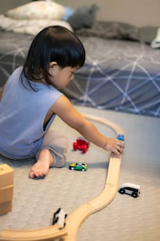 Little boy in a blue shirt sits on the floor playing with a blue train on a wooden track. Education concept.