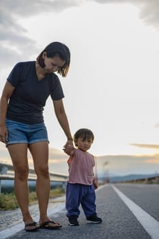 Mother and her toddler are standing on a road.