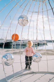 Little girl stands near a Christmas installation with mirror balls. High quality photo