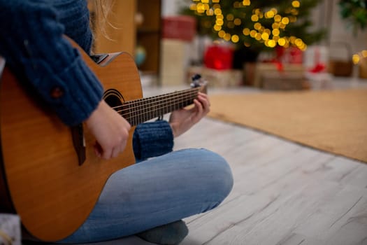A person joyfully plays an acoustic guitar in a warm, festive setting adorned with beautiful holiday lights