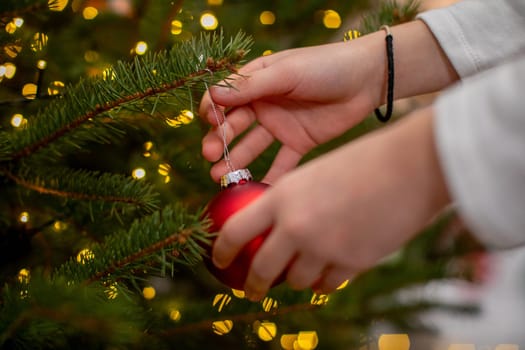Closeup of hands hanging a red ornament on a beautifully decorated Christmas tree with twinkling lights
