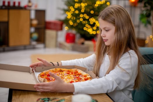 A young girl filled with joy eagerly opens a delicious pizza box in a cozy room decorated for the holiday season