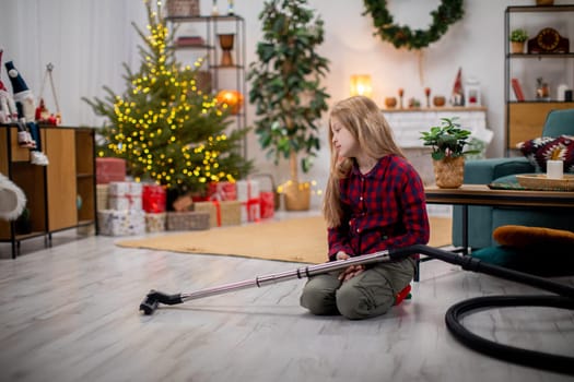A young girl kneels down with a vacuum cleaner in a festive living room that is beautifully adorned for the holidays