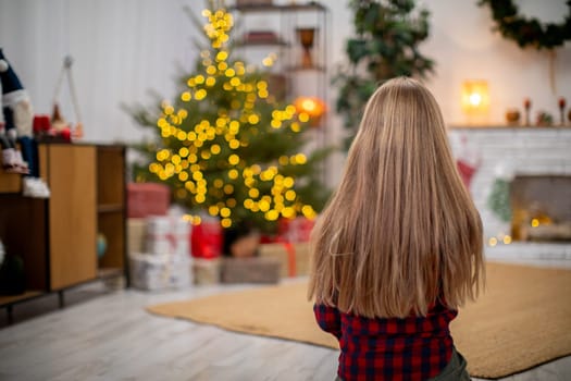 A girl happily enjoys a warm and cozy Christmas evening by the beautifully decorated tree with bright lights