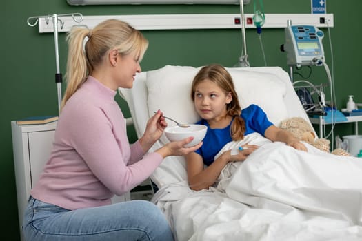A caring mother feeds her daughter in a hospital bed, offering comfort and support during this challenging time