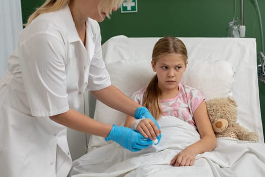 A young girl in a hospital bed receiving care from a nurse. Comforting atmosphere with a teddy bear.