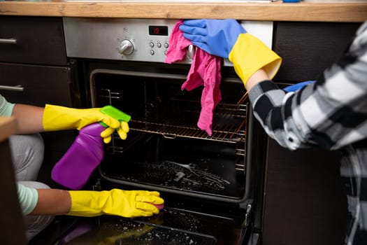 Two individuals clean an oven together, showcasing teamwork and effective cleaning tools that aid the process