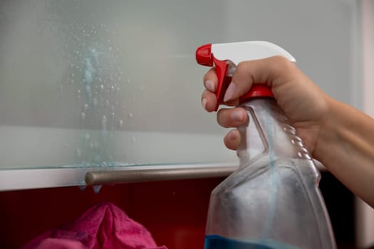 A person diligently cleaning a glass surface using a spray cleaner to achieve a perfectly spotless shine