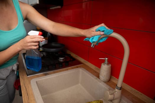 A person is diligently cleaning a kitchen faucet using a spray cleaner and a cloth in a modern, stylish kitchen