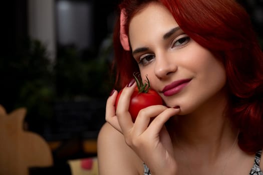 A lively young woman with striking red hair playfully holds a fresh tomato, exuding joy and creativity