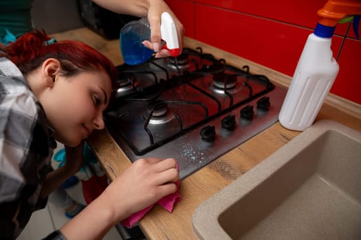 A woman is diligently cleaning a gas stove in a beautifully styled kitchen using various cleaning supplies