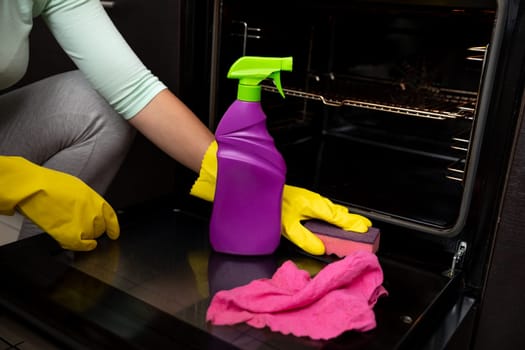 A person cleaning an oven with a colorful spray bottle and cloth, showcasing effective kitchen maintenance.