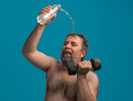 A dedicated elderly man focuses on his workout as he curls dumbbells with one hand while splashing water on his head with the other hand, enjoying a refreshing moment.