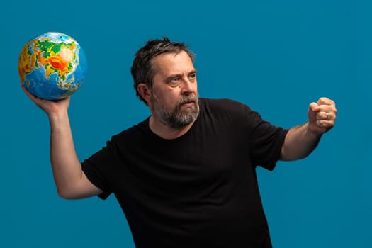 Fragility and vulnerability of the world concept.A bearded man stands confidently, holding a vibrant globe in one hand while his other fist is raised. 