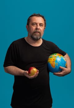 A middle-aged man stands confidently against a bright blue background, holding an apple in one hand and a globe in the other, embodying the connection between knowledge and nature.
