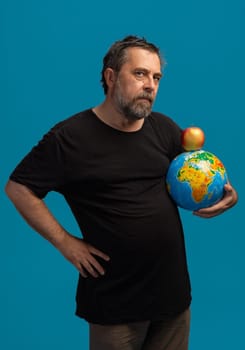 A thoughtful man stands confidently with a colorful globe in one hand and a bright red apple balanced atop it.