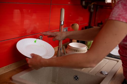 A person is thoroughly cleaning a gleaming white plate at a sink located in a stylish and vibrant red kitchen