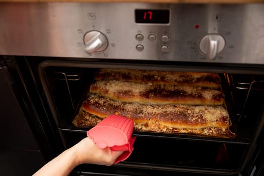 A hand wearing a silicone mitt is carefully reaching into a hot oven to retrieve some freshly baked goods