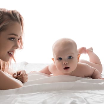 A mother smiles at her baby lying on a white surface, captured in a joyful interaction during a sunny day.