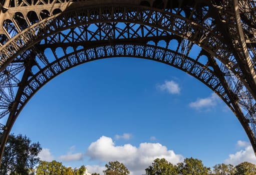 A stunning view of the iconic Eiffel Tower arch set against a serene blue sky with fluffy white clouds floating by