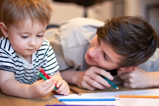 Two children draw with colored pencils. A teenager and a younger brother draw while lying on the floor. High quality photo