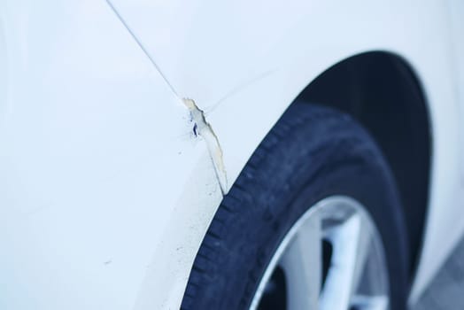 There is damage that can be seen on the fender of a white car, specifically near the tire area