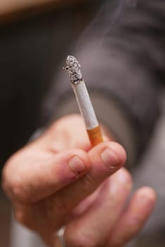 A hand is firmly grasping a lit cigarette, which is producing smoke that rises into the air