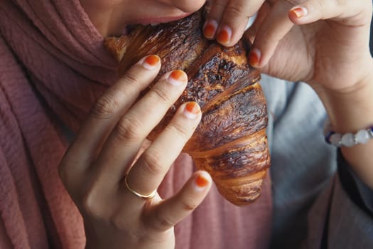 A woman is savoring a warm and delicious croissant while sitting in a cozy and inviting setting