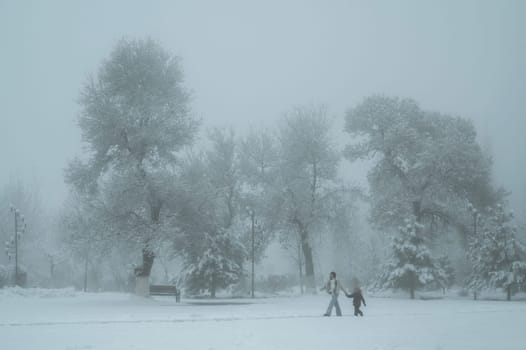 woman mother and a child son walk through the Independence Park in Shymkent in Kazakhstan in winter with snow and fog