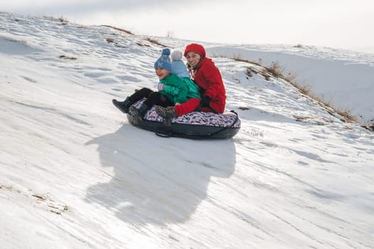 TAU SAMALY, KAZAKHSTAN - DECEMBER 23, 2023: happy Kazakhs family tubing down a slide in winter with snow at the Tau Samaly recreation center in Kazakhstan