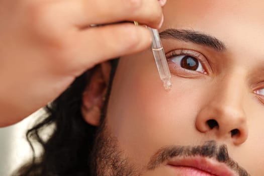 A close-up of a man applying a serum drop to his face, showcasing skincare routine