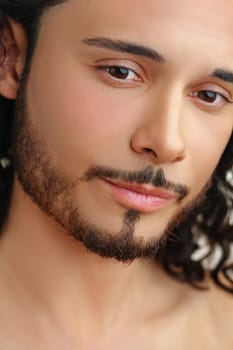 Close-up portrait of a man with long curly hair and a well-groomed beard showcasing clear skin