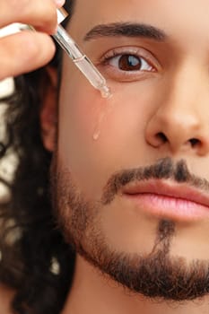 A close-up of a man applying a serum drop to his face, showcasing skincare routine