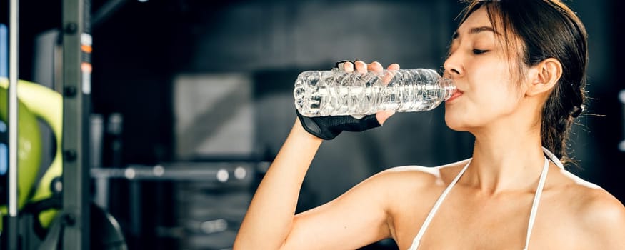 Asian woman guy hydrated by drinking water sports from a bottle in gym after cardio work out, female tired with liquid bottle drink after training at fitness gym, workout healthy lifestyle concept