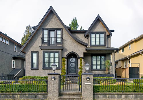 Gloomy residential house with metal fence in front on overcast sky background.