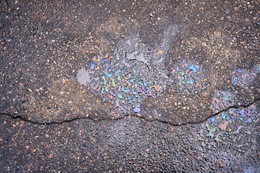 Colorful gasoline or oil spill creating a rainbow effect on cracked asphalt road surface