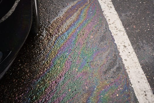 Colorful gasoline or oil spill creating a rainbow sheen on wet asphalt road near a car, illustrating environmental pollution