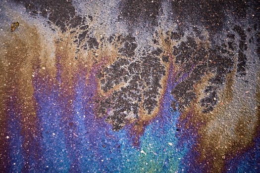Colorful gasoline or oil spill creating a rainbow chemical reaction on asphalt road surface.