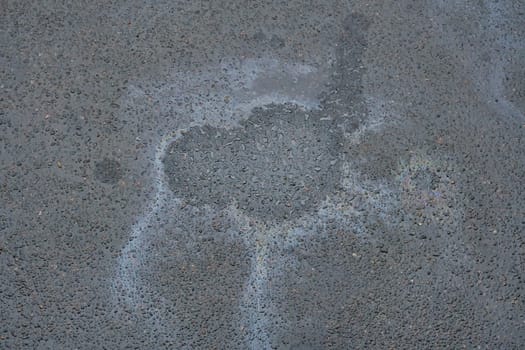 Gasoline or oil spill creates rainbow chemical sheen on asphalt road surface.