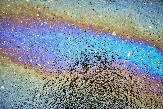 Colorful gasoline spill creating a rainbow effect on asphalt road.